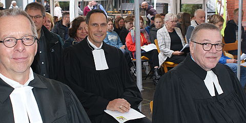 Das Bild zeigt Pfarrer Dr. Ralf Stroh, Dekan Steffen Held, Oberkirchenrat Detlev Knoche. Sie sitzen im Talar in der ersten Reihe beim Eröffnungsgottesdienst.
