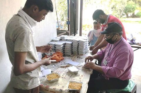 Das Bild zeigt Männer in Indien, die verzehrfertige Mahlzeiten zum Mitnehmen für Bedürftige verpacken.